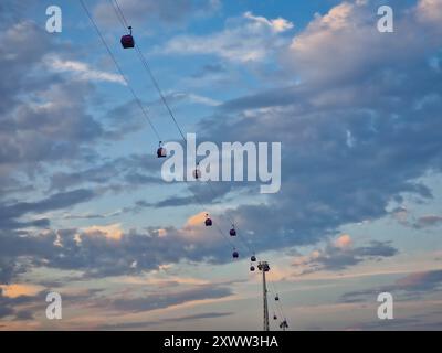 a wide, low-angle shot of numerous small cable car gondolas suspended along a pair of diagonal overhead wires. Stock Photo