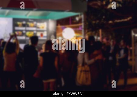 A blurred image of a crowd of people standing in front of a building in Hong Kong at night. The bokeh background suggests a bustling urban environment Stock Photo