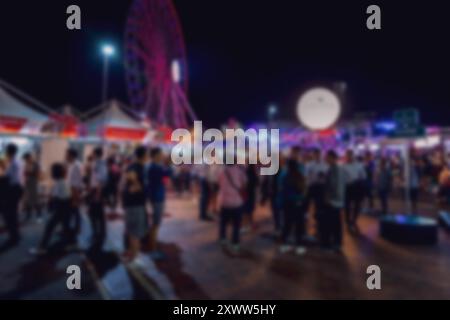 Blurry night scene of a crowd gathered at a Hong Kong night market with a ferris wheel in the background. Stock Photo