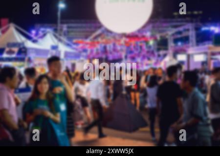 A blurred image of a crowd of people walking at night. The background is blurred with lights, creating a bokeh effect. Stock Photo