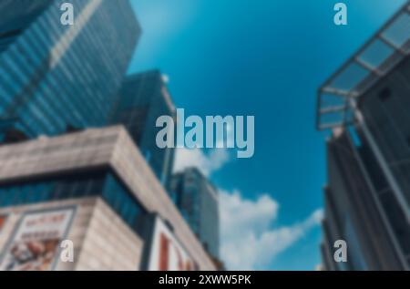 A blurred image of tall buildings against a bright blue sky with white clouds. Stock Photo