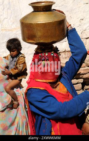 A big smile under the veil. A Rajasthani woman comes back home with a brass water vessel on her head. Photo taken in the outskirts of Nagaur, India. Stock Photo