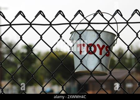 silver tin toy bucket hanging on black chain link fence Stock Photo