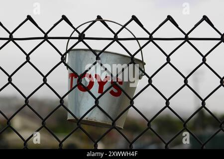 silver tin toy bucket hanging on black chain link fence Stock Photo