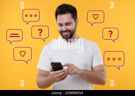 Happy man sending message via smartphone on orange background. Speech bubbles near him Stock Photo