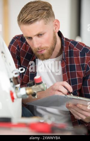 view of plumber writing in clipboard while checking electric boiler Stock Photo
