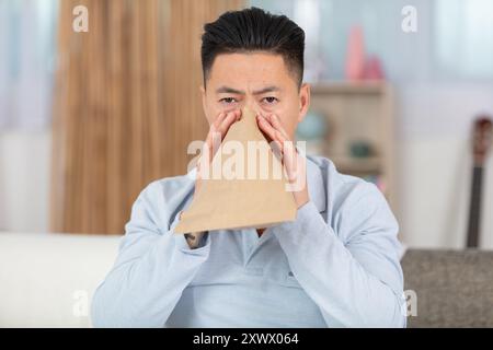 stressed man breathing with paper bag while having panic attack Stock Photo