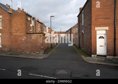 Brick houses lining a narrow alleyway in Wallsend, Newcastle upon Tyne. The image captures the essence of quiet, residential life with a nostalgic feel. The empty street and red-brick walls provide a sense of community and history. Stock Photo