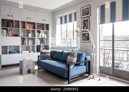 Pale blue sofa with striped blinds and bookcase in stylish modern, classic home in London, UK Stock Photo
