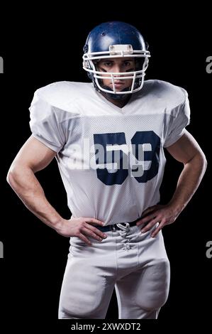 American football player. American football player looking at camera and holding hands on hips while standing against black background Stock Photo