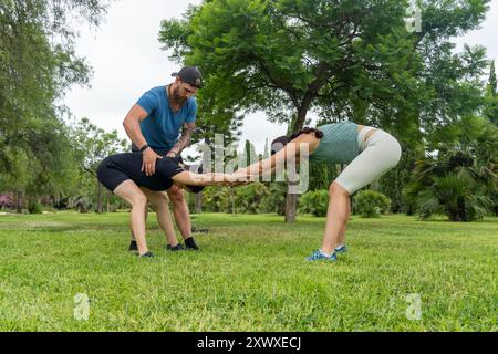 A personal trainer assists two women during a partner stretching exercise in a park, emphasizing teamwork and flexibility in an outdoor fitness sessio Stock Photo