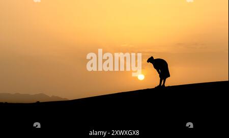 Silhouette of unidentified muslim Berber man praying on sand dunes at ...