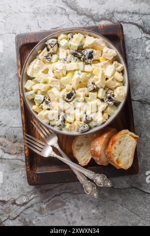 Salad with chicken, prunes, boiled eggs and fresh cucumber dressed with mayonnaise close-up in a bowl on a wooden board. Vertical top view from above Stock Photo