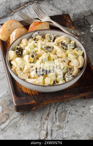 Salad with chicken, prunes, boiled eggs and fresh cucumber dressed with mayonnaise close-up in a bowl on a wooden board. Vertical Stock Photo