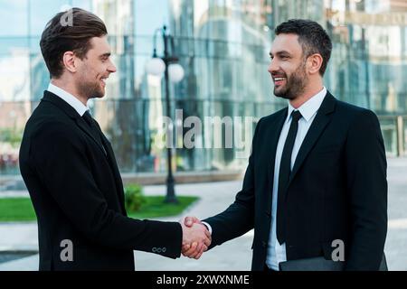 Men handshaking. Two confident young businessmen shaking hands and smiling while standing outdoors Stock Photo