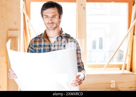 Reviewing the plan. Confident young man looking through blueprint while standing at his workshop Stock Photo