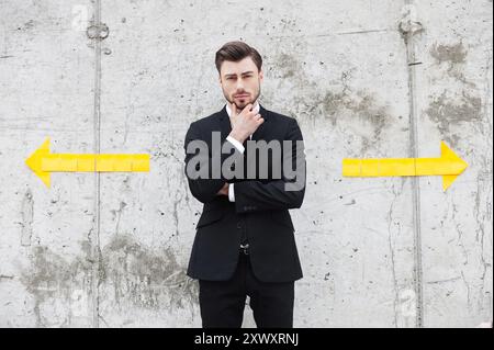 Facing the choice. Thoughtful young man in formalwear holding hand on chin while standing outdoors Stock Photo