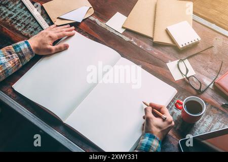 Start planning today. Close-up top view image of man writing in notebook with copy space while sitting at the rustic wooden table Stock Photo