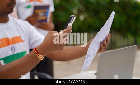 Young Indian man paying bills using mobile and laptop. QR code scan and pay concept. Work from home Stock Photo