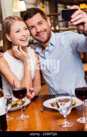 Capturing romantic moments. Beautiful young loving couple making selfie and smiling while sitting at the restaurant together Stock Photo