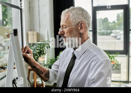 A middle-aged, bearded man writes on a whiteboard while teaching an online class. Stock Photo