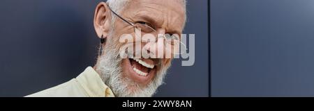 A bearded man with glasses laughs outdoors in front of a modern building. Stock Photo