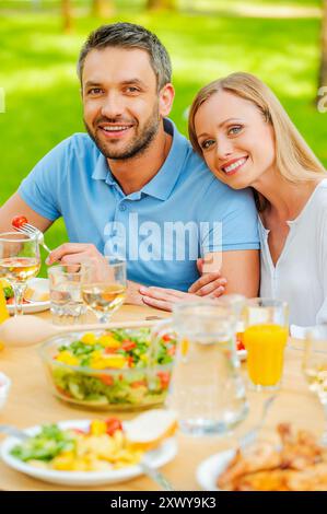 Dinner at the fresh air. Top view of happy young loving couple enjoying meal together while sitting at the dining table outdoors Stock Photo