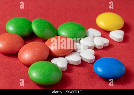 Close-up of a handful of heart-shaped pills and colored dragees on a red background. Stock Photo