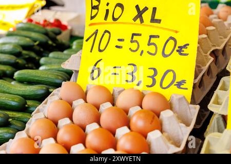 Fresh organic brown eggs in paper cartons box at local farmers market sale. Bright yellow sign showing prices. Local domestic organic regional natural Stock Photo