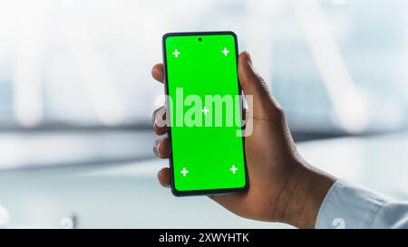 Anonymous Businessman Holding Smartphone with Green Screen Mock Up Display, Making a Video Call in a Professional Office Environment. Virtual Meetings, Modern Technology and Connectivity Concept Stock Photo