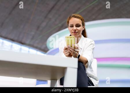 Caucasian young adult businesswoman sits in the office centre and using her smart phone, reading message. Stock Photo