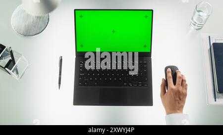Anonymous Corporate Employee Using Laptop Computer with Mock Up Green Screen Chromakey Display with Placeholders. Man Sitting Behind a Desk, Browsing Internet, Using a Wireless Mouse. Top Down View Stock Photo
