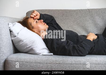 Tired and depressed woman lying down on the sofa. Mental problems, anxiety, overworking. Stock Photo