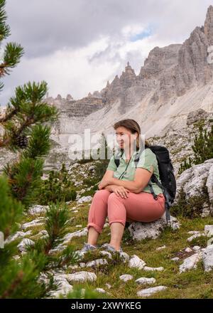 Female traveler in her 50s enjoys a trip in mountains. Magnificent views.Woman sitting on a rock. Healthy lifestyle, hiking Stock Photo