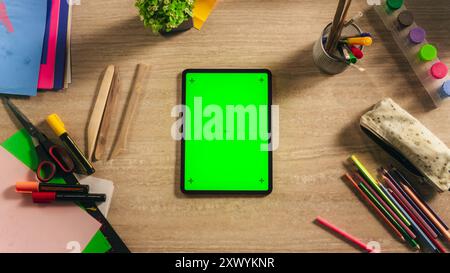 Top View of a Tablet Computer with Vertical Mock Up Green Screen Chromakey Display with Motion Trackers Lying on a Designer's Desk Next to Colorful Pencils, Markers, Art Supply Tools for Illustrators Stock Photo