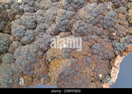A close-up of a dark, textured mineral surface with bumpy, rounded formations displaying subtle iridescent colors, including hints of green, blue, and Stock Photo
