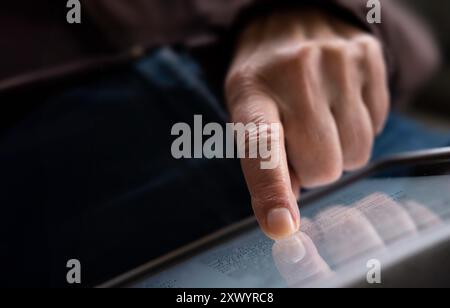 Reading. Close-up of finger on the touchscreen of a tablet with dark background and reflection of the fingers in the screen. Focus on the index finger Stock Photo
