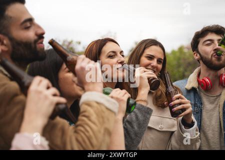 Group of diverse young adults enjoying beer together outdoors. Millennial friends socializing, celebrating and having fun. Concept of friendship, dive Stock Photo