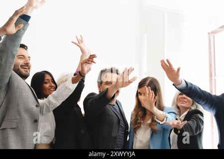 Diverse group of business professionals celebrating success with raised arms. Multi-ethnic and multi-generational team joy and unity in bright office Stock Photo
