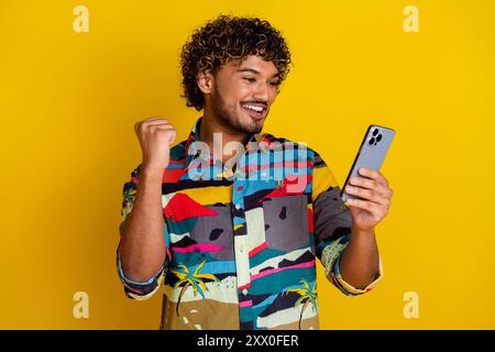 Photo portrait of handsome young male hold device winning dressed stylish colorful garment isolated on yellow color background Stock Photo