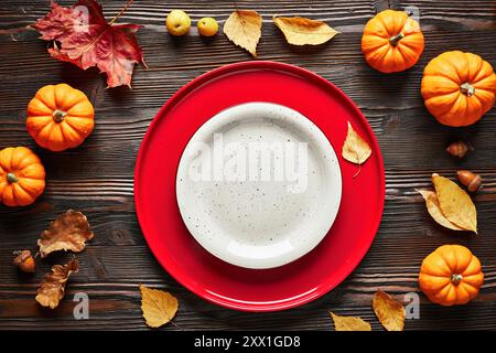 Empty red and white plates on dark wooden background in autumn decor, top view. Stock Photo