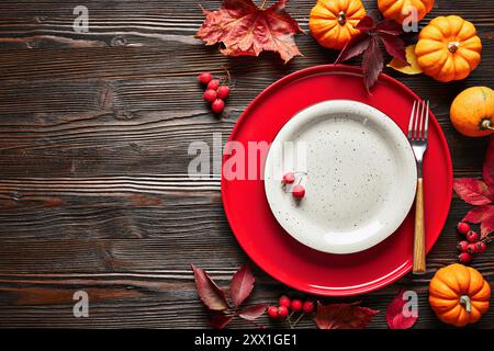 Empty red and white plates on dark wooden background in autumn decor, top view. Stock Photo