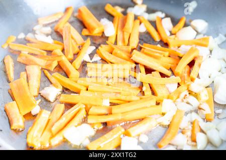 Carrots and onions are fried in a chrome pan. Ingredients for cooking a dish according to the recipe. High quality photo Stock Photo