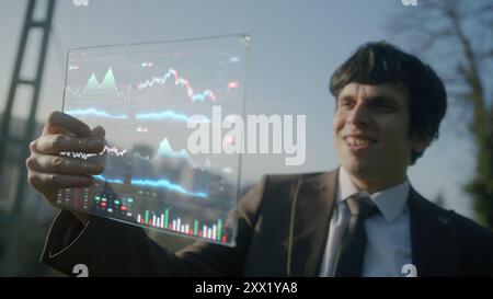 Man in suit conducting finance business with futuristic touch screen holographic glass table outdoors. AI, big data, software, finance, cryptocurrency Stock Photo