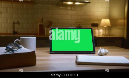 Tablet computer with green mock up green screen on table with a book and notebook in the cozy kitchen. Stock Photo