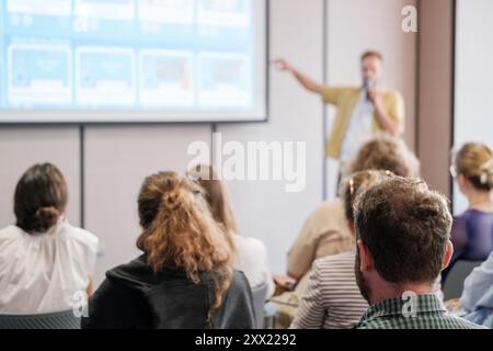 Group of people engaged in a professional seminar with speaker presenting at front. Audience focused on learning. Stock Photo