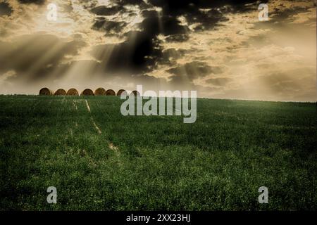 Sunlight streaming through dark clouds over hay bales in a field at sunset, Sarezzano, Tortona, Alessandria, Piedmont, Italy Stock Photo