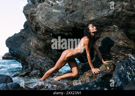 Side view of an Athletic Woman in a bikini exercising on coastal rocks, Spain Stock Photo