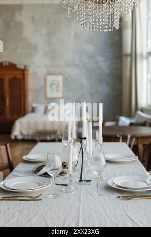Elegant dinner table setting with a fresh loaf of bread for four people in a stylish open plan apartment with a bed in the background Stock Photo