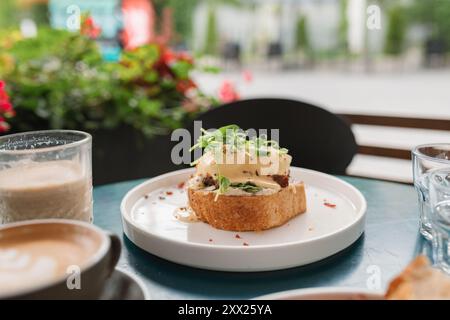 Close-up of a slice of toast with poached eggs, bacon and cheese sauce with pea shoot garnish Stock Photo